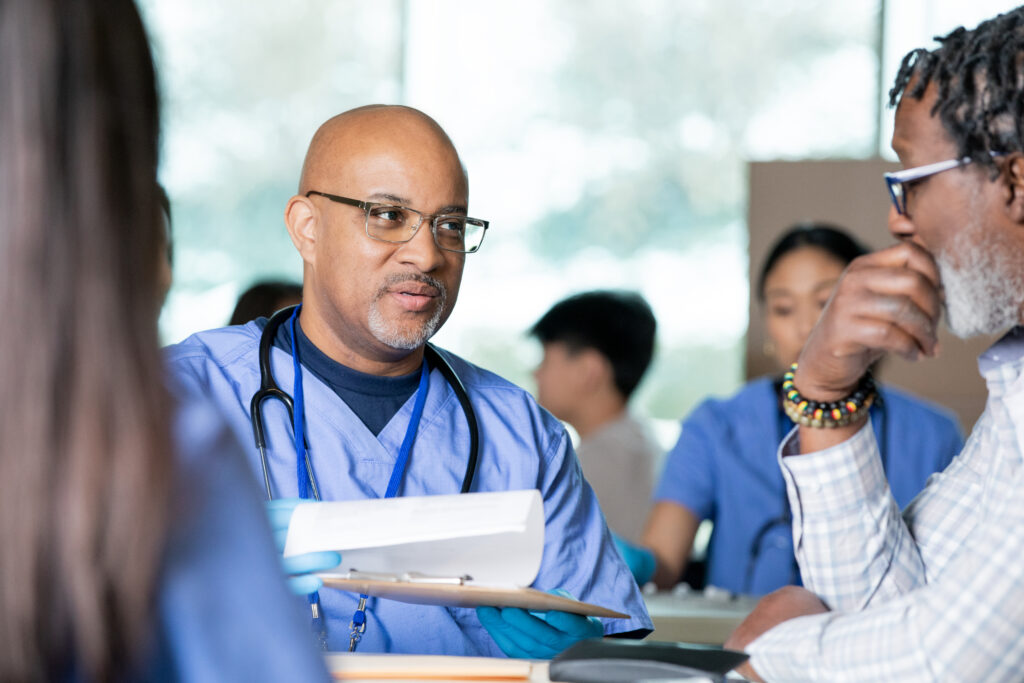 Doctor volunteers at community health fair and consults patient charts while meeting with senior patient